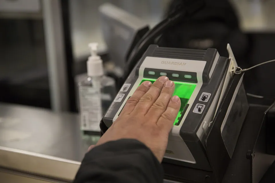 A hand placed flat on an illuminated fingerprint scanner at a service desk