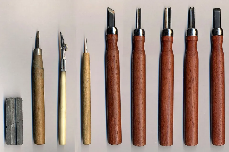 A row of wood-carving chisels and gouges with wooden handles laid out beside a sharpening stone
